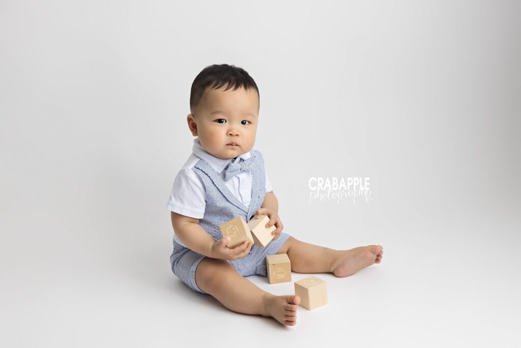 10-month-old baby boy in bowtie sitting for a portrait and playing with blocks in a light and airy studio