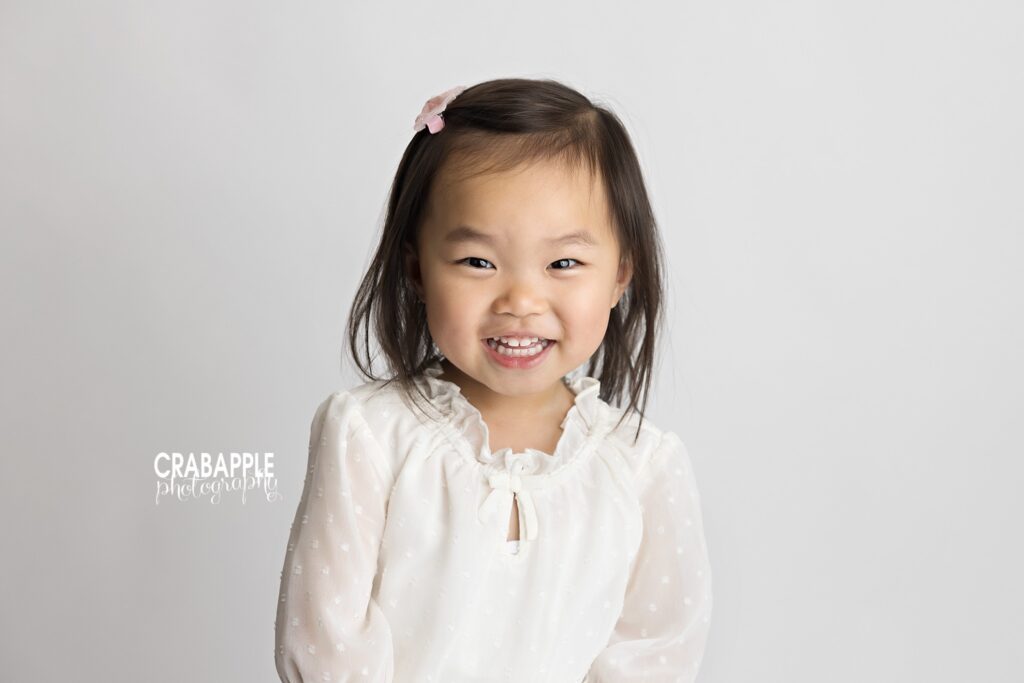 Older 3 year old sister smiles for camera during milestone baby photo session