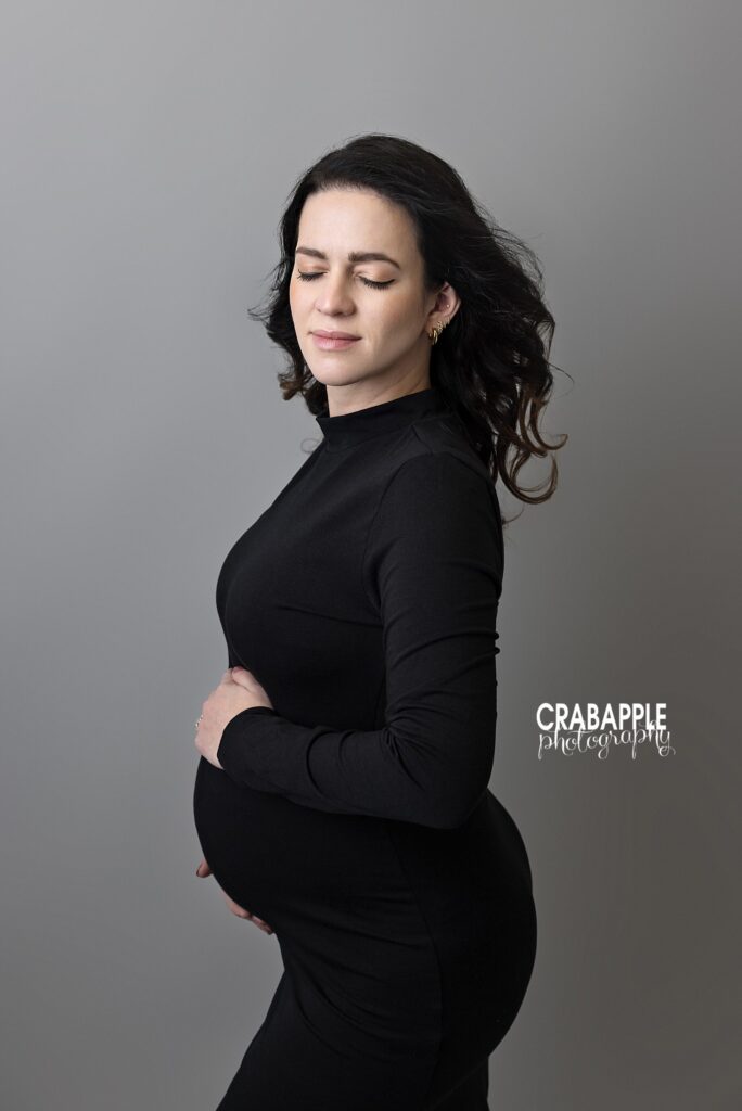 Elegant black dress maternity portrait Elegant maternity portrait of an expecting mother in a fitted black dress against a gray studio backdrop