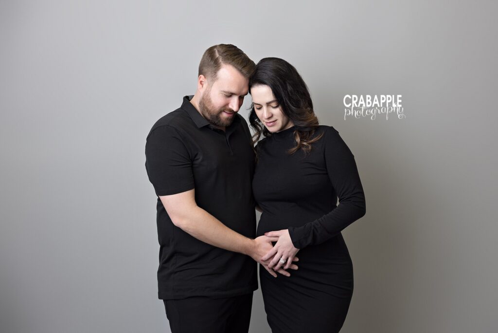 Black outfit maternity couple portrait Expecting couple wearing black outfits in front of a light gray studio backdrop