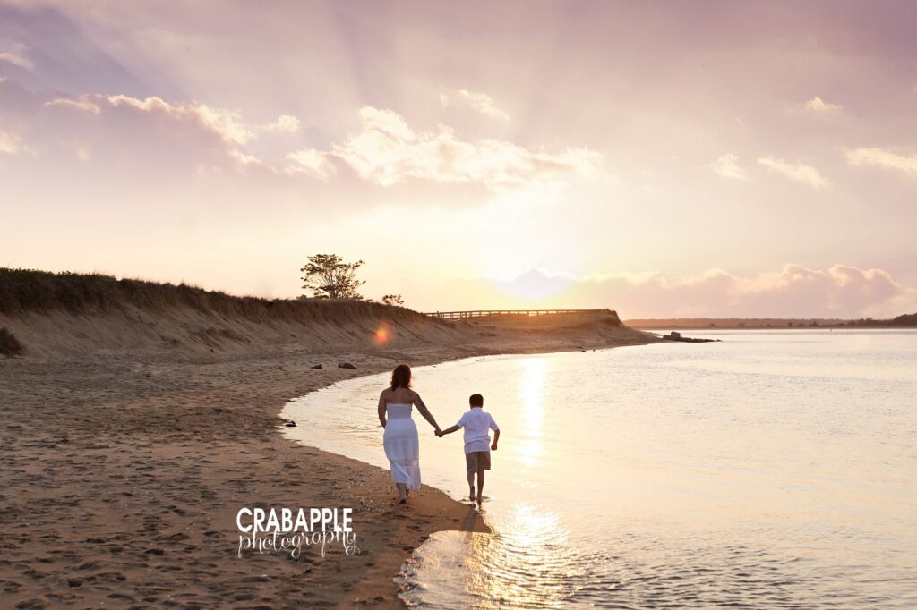 mom and son walk through the water during sunset for beach family photos
