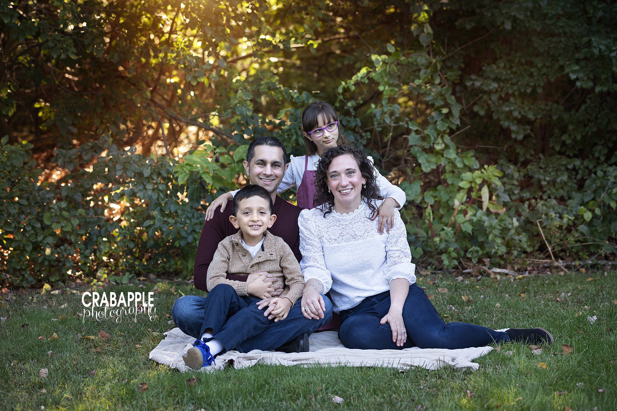 Family of four pose together outdoors on the ground during fall family portraits