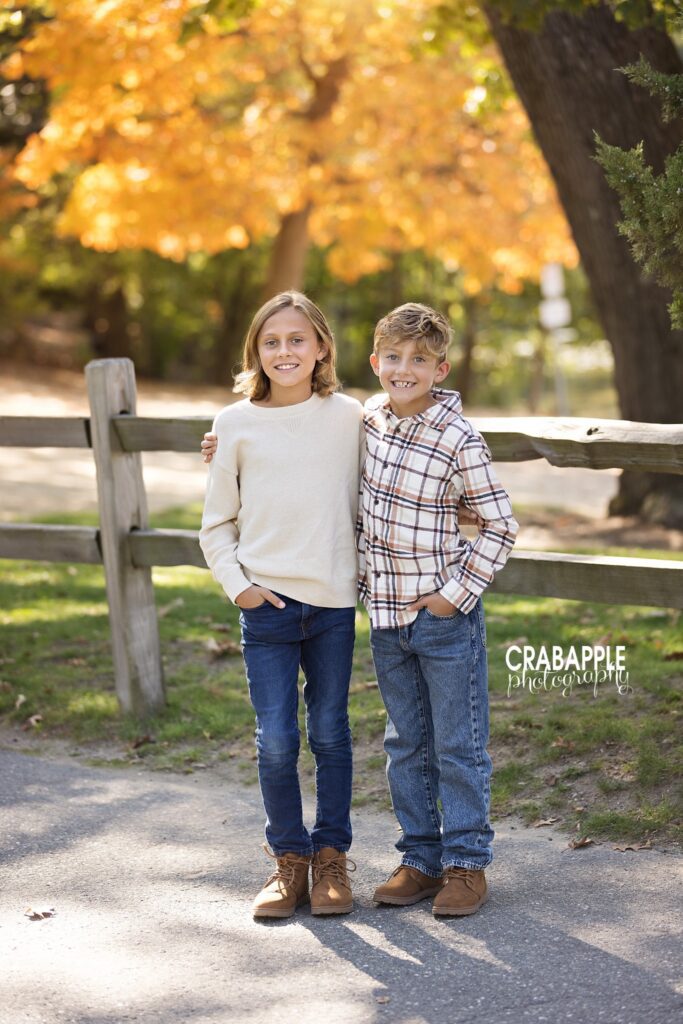 Two brothers standing together on a wooded path surrounded by fall foliage in Medford
