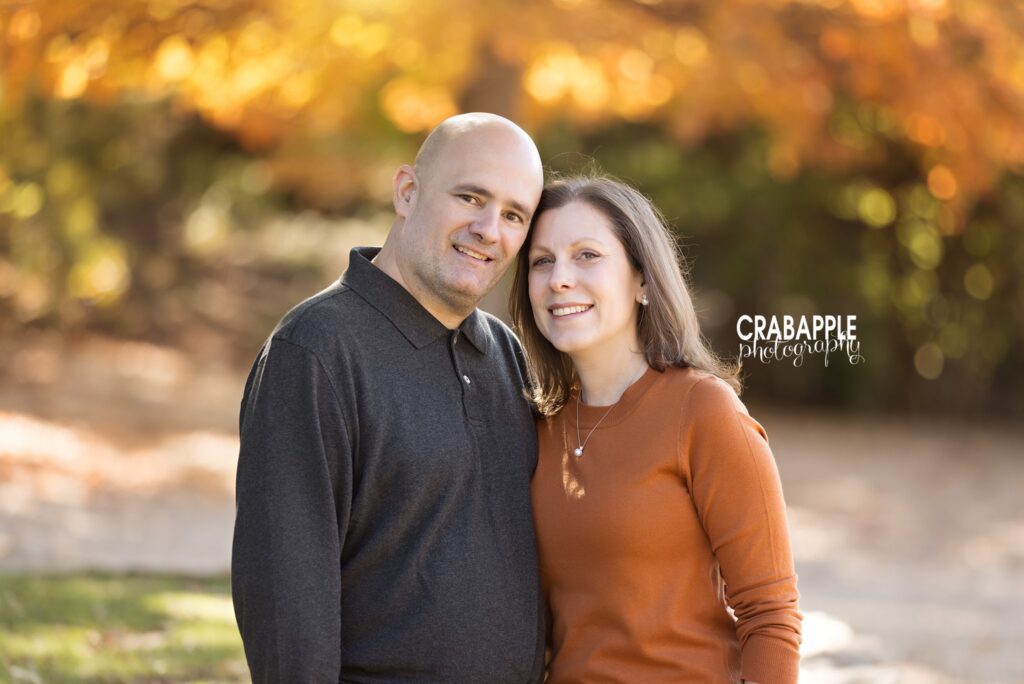 Couple standing together outdoors surrounded by warm autumn foliage in Medford