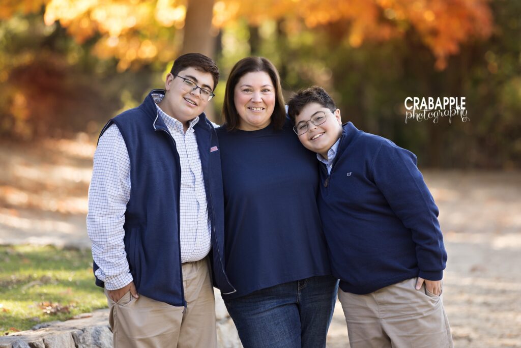Mother and sons in coordinating outfits pose together during outdoor fall family portraits in Medford MA