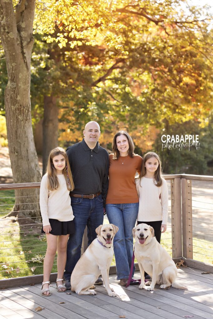 Family standing together with dogs on a wooded path surrounded by colorful fall foliage in Medford