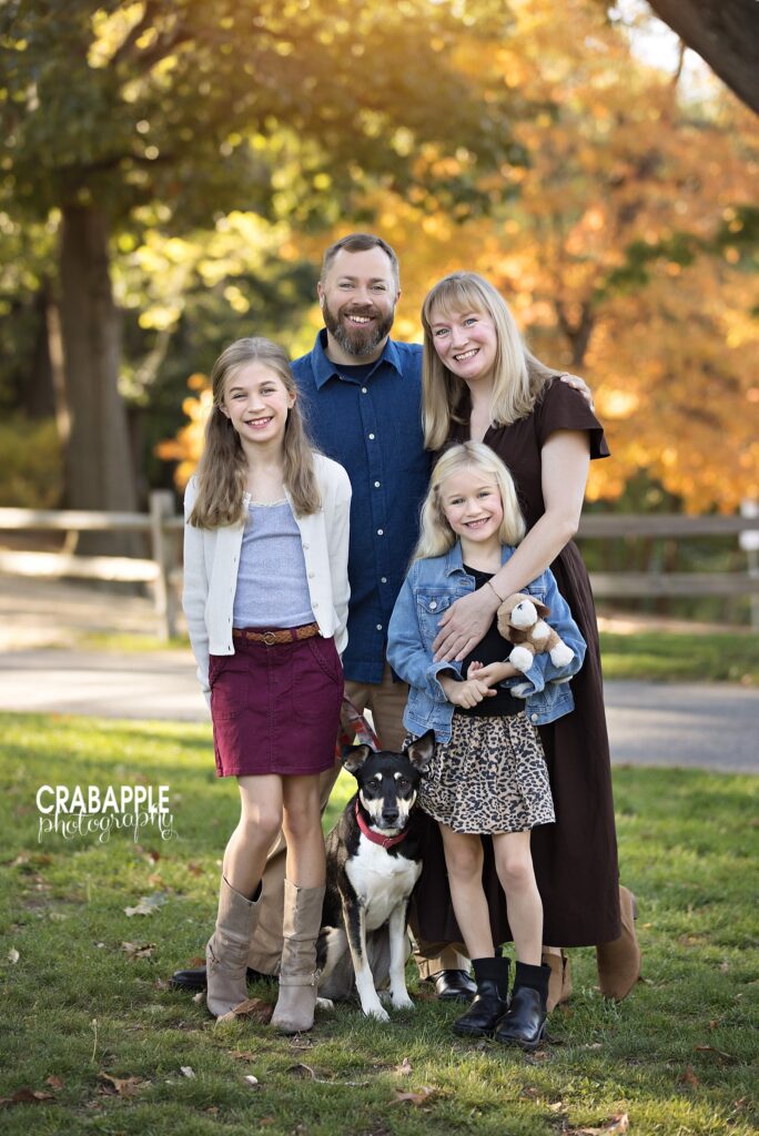 Family standing together outdoors beneath colorful autumn trees in Medford with pet dog