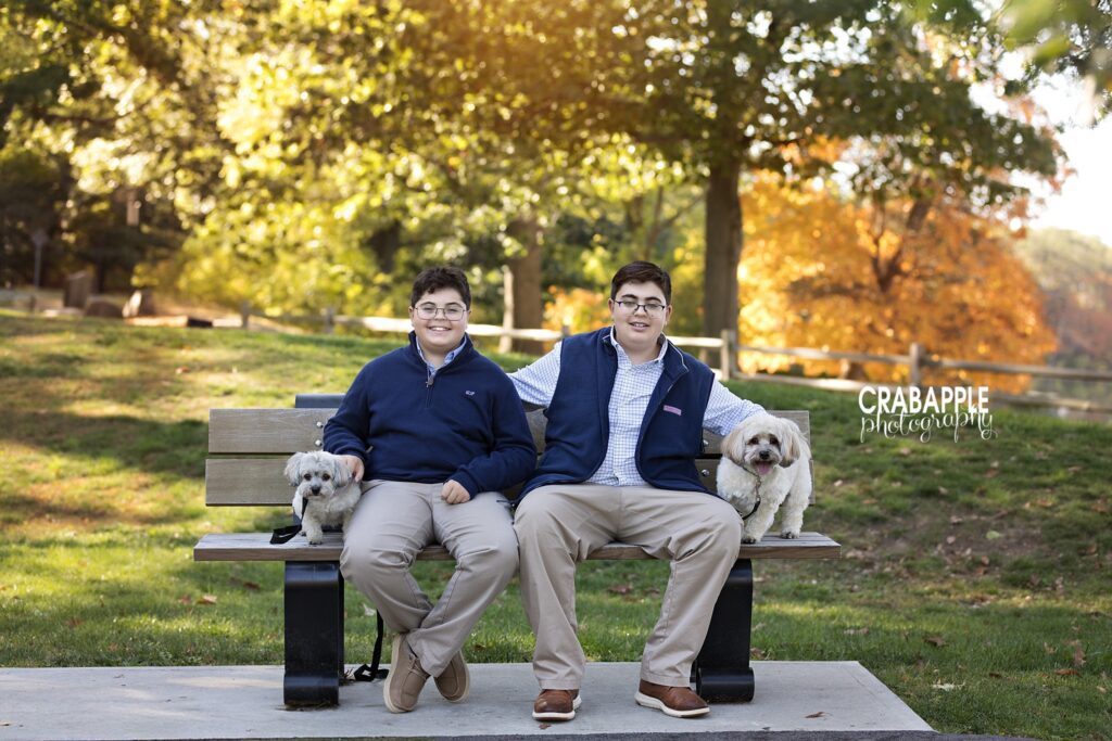 Two brothers sit on a bench with their family dogs during a Medford MA fall family portrait session