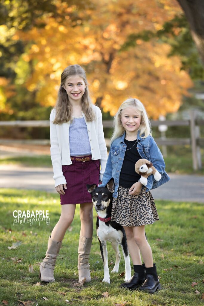 Sisters during autumn park photos Two sisters standing together with a small dog during fall photos in a Medford park