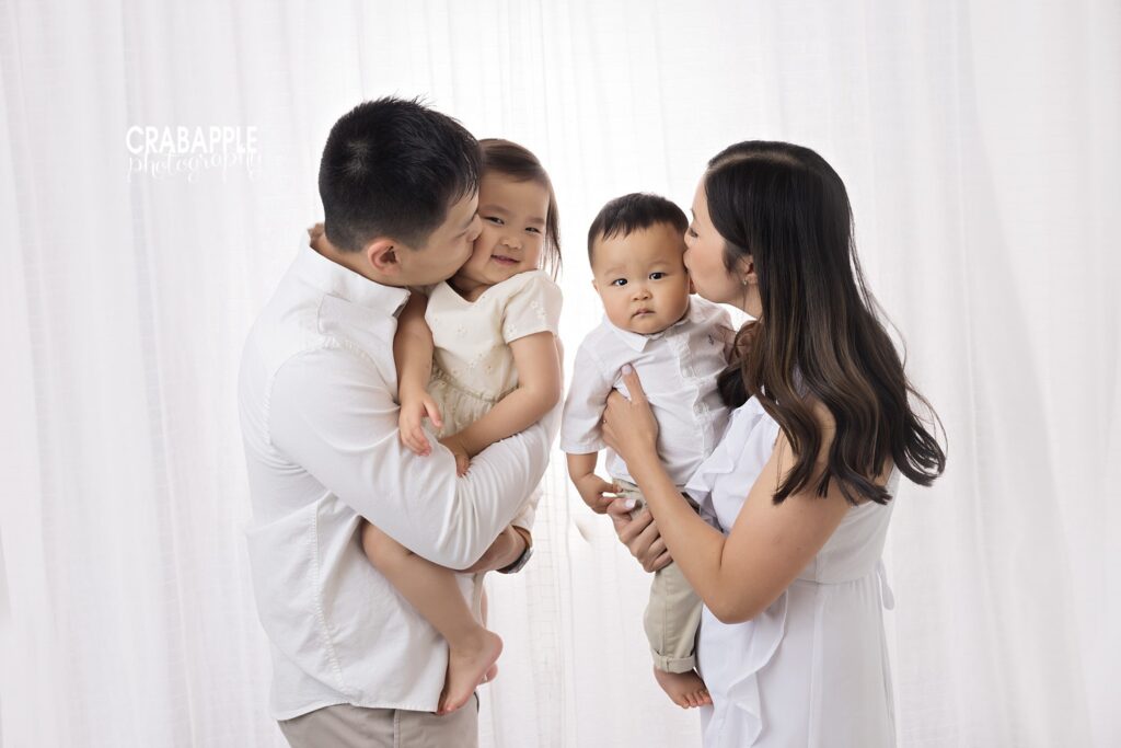 Parents giving their two children a kiss during milestone baby photography session in Andover MA
