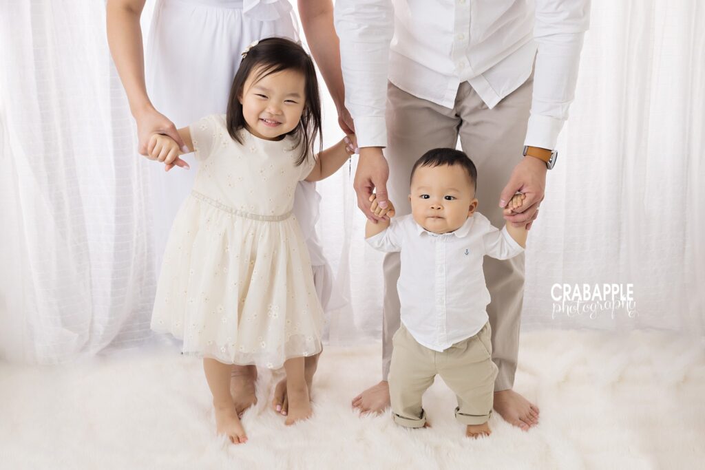 Mom and dad each old the hands of one of their children during milestone baby and family portrait session