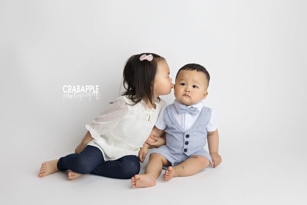 Three-year-old girl giving 10 month old baby brother a sweet kiss during a studio milestone session