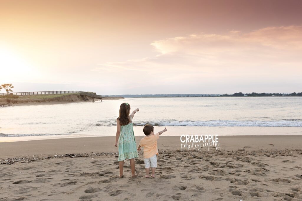 two siblings stand by the shore and point out to the water during family beach photos