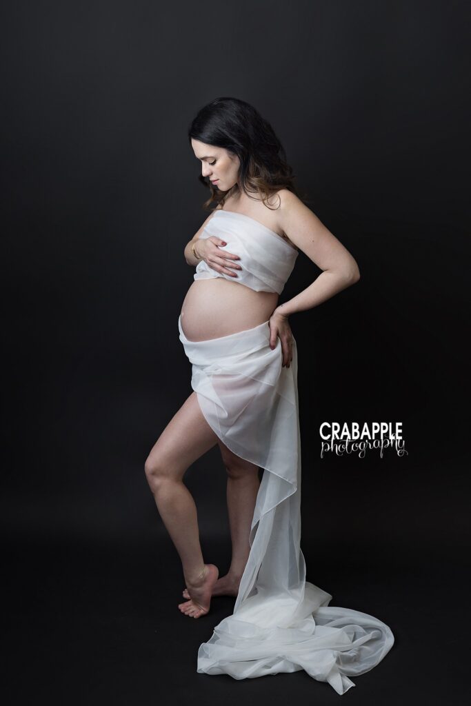 Draped fabric maternity portrait Artistic maternity portrait of an expecting mother wrapped in draped fabric against a black backdrop
