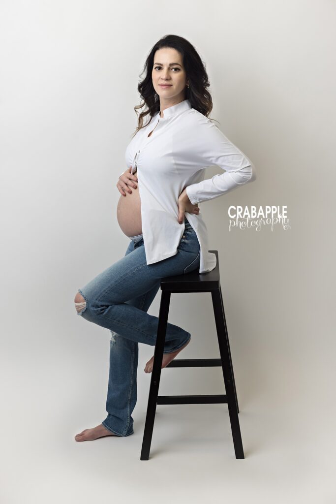 Casual maternity portrait on stool Expecting mother sitting on a studio stool wearing jeans and a white top