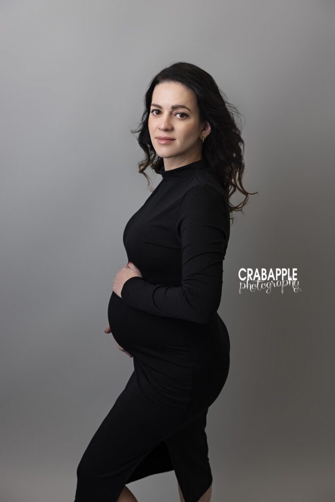 Black dress maternity portrait in studio Expecting mother in a fitted black dress during a studio maternity session with a gray backdrop