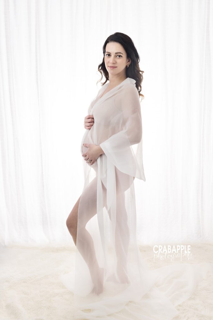 Sheer white robe maternity portrait Expecting mother wearing a sheer white robe in soft studio lighting during her maternity session