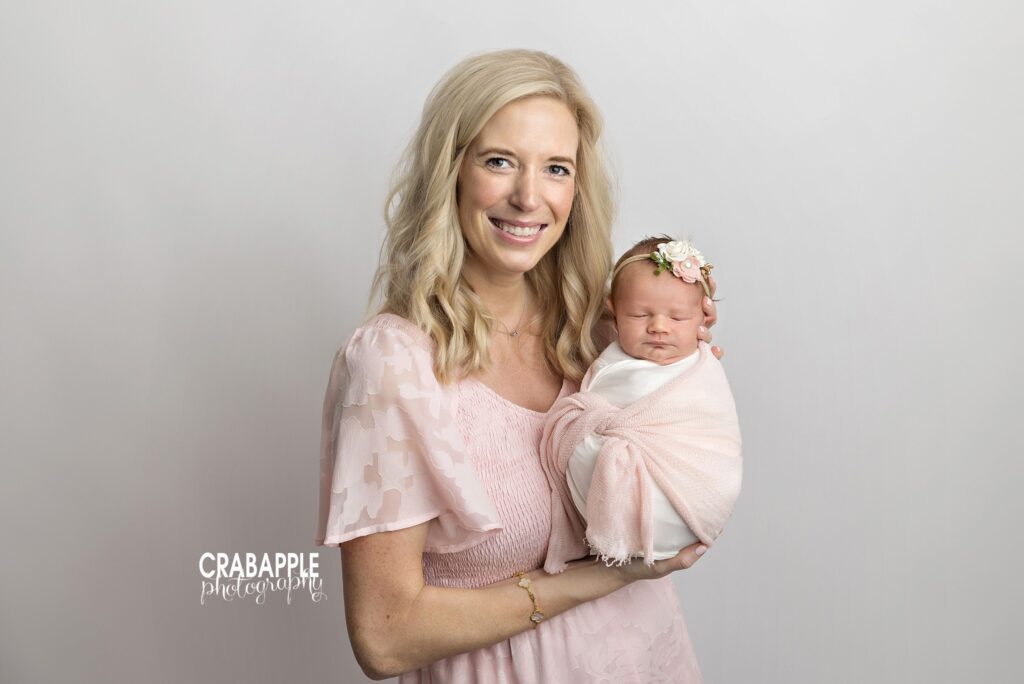Mother smiling as she holds her newborn baby girl in a soft pink outfit
