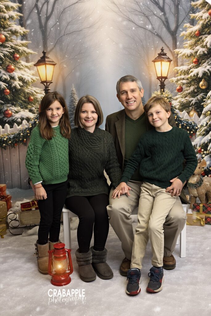Family dressed in coordinated green and neutral outfits posing in front of a decorated Christmas set	