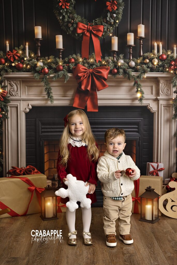 Two siblings posing together in front of a decorated fireplace during a Christmas mini session	
