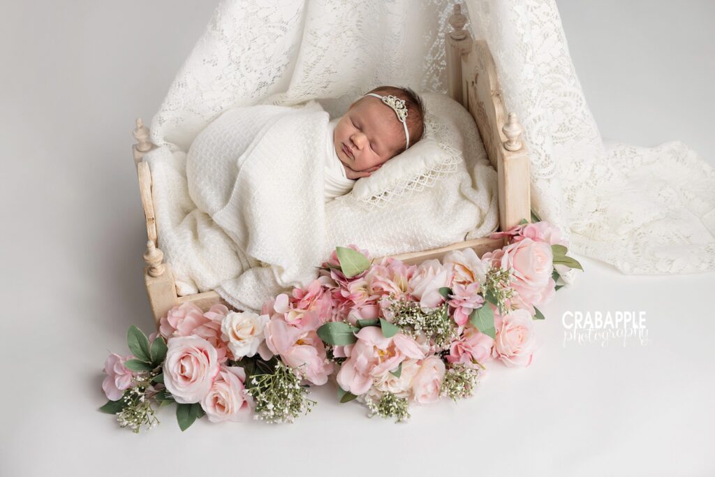 Sleeping newborn baby girl posed in a delicate vintage-inspired bed with lace and pink flowers

