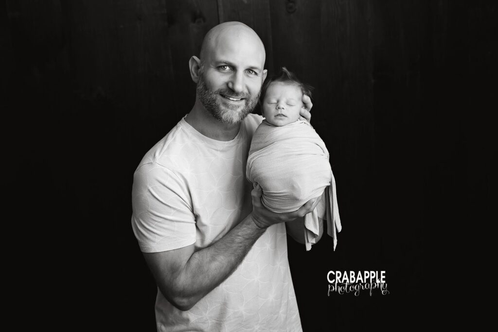Newborn baby boy held close by his father in a black and white portrait

