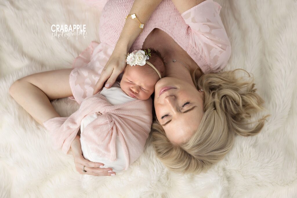 Mother lying down and cuddling her newborn daughter close to her face in a soft pink outfit

