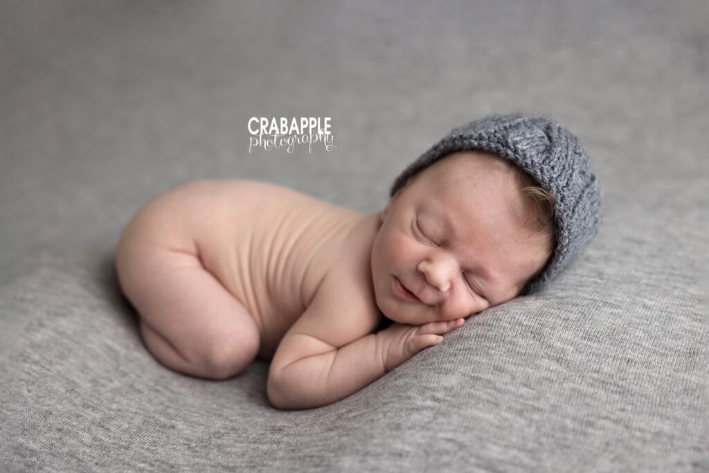 Newborn baby boy posed with his bottom in the air wearing a gray knit beanie
