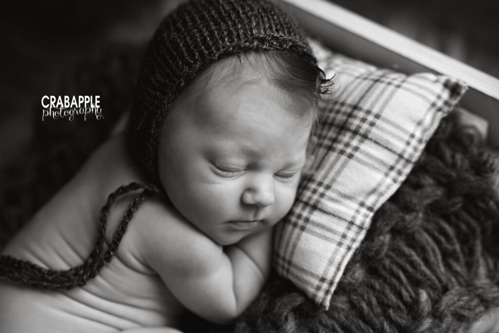 Newborn baby boy sleeping on a small wooden bed in a black and white portrait
