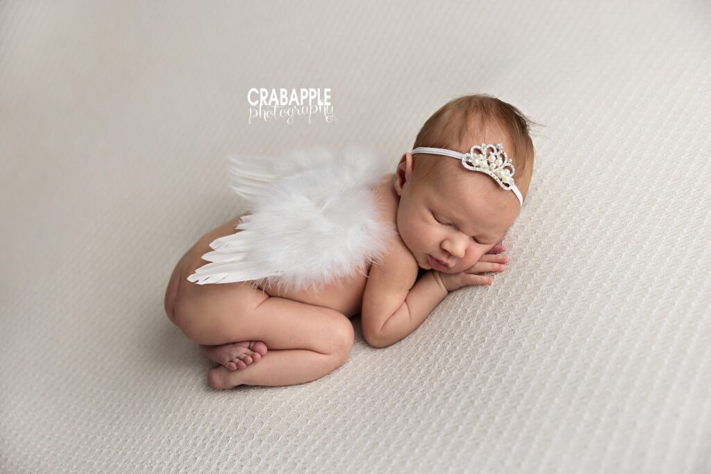 Newborn baby girl resting on her belly with a delicate tiara headband and soft angel wings
