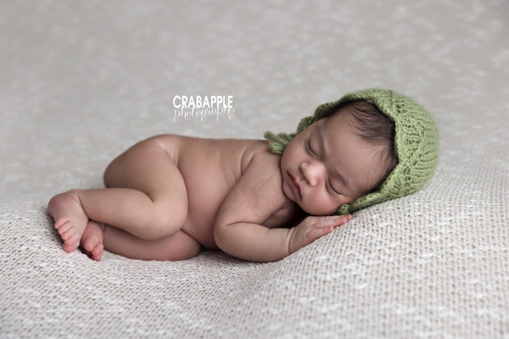 Side-lying portrait of a newborn girl wearing a soft light green knit bonnet	