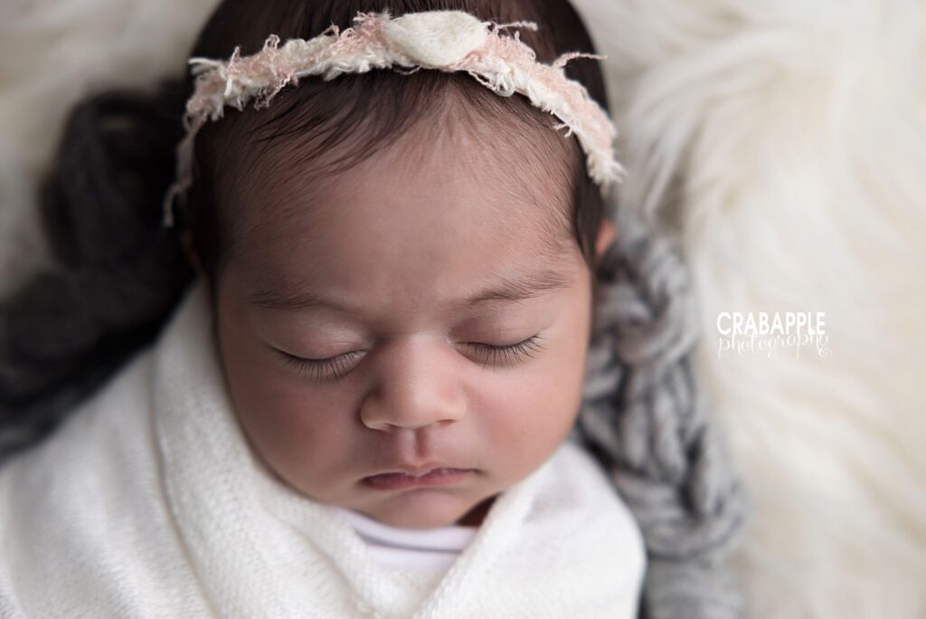 Close-up of a newborn girl's face framed by a white swaddle and delicate headband	
