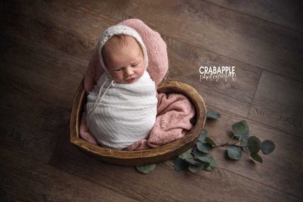 Newborn baby girl wrapped in a soft swaddle and sleeping in a heart-shaped wooden bowl
