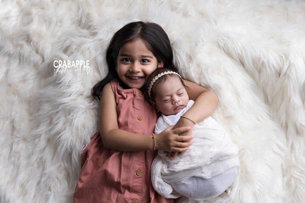 Toddler sister posing peacefully with sleeping newborn sister
